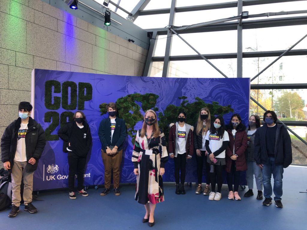 Group of people with facemasks stand outside a sign that says COP26